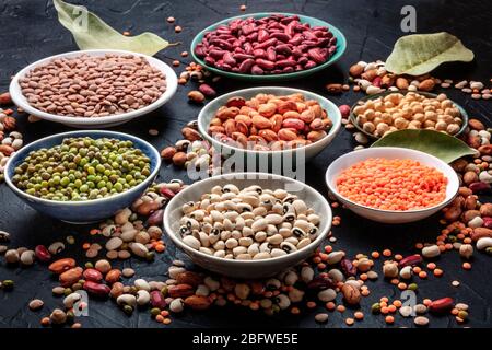 Assortimento di legumi su sfondo nero. Lenticchie, fagioli di soia, ceci, fagioli rossi, una ventietà di impulsi Foto Stock