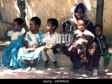 1993 - diritto sul colpo di cinque bambini somali e un somalo donna come loro siedono su un cordolo aspettando pazientemente il loro turno per vedere US Navy medici conducendo un medico civile Programma d'azione nella capitale Mogadiscio, Somalia. Foto Stock