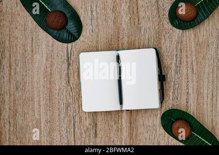 Blocco note con carta bianca, distesa, giace su uno sfondo di legno, una penna sul retro di un notebook. Biscotti al cioccolato per colazione. Vista dall'alto, piatto, Foto Stock