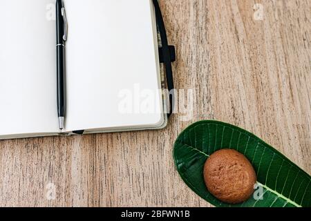 Blocco note con carta bianca, distesa, giace su uno sfondo di legno, una penna sul retro di un notebook. Biscotti al cioccolato per colazione. Vista dall'alto, piatto, Foto Stock