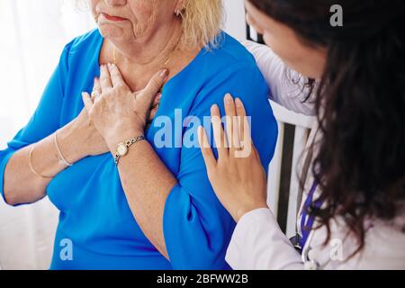 Donna anziana lamentandosi della respirazione lavorata quando il medico la visita a casa Foto Stock