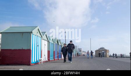 Brighton, Sussex, Regno Unito - 8 marzo 2020: Persone che camminano con un cane lungo il lungomare di Hove con capanne colorate sulla spiaggia in inverno Foto Stock