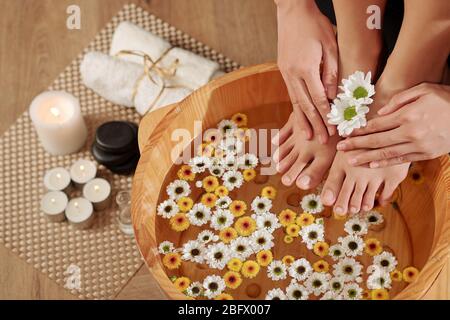 Donna che mette i piedi in bacinella di legno con acqua e piccoli fiori per fare pedicure Foto Stock