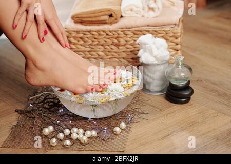 Donna che prende il bagno di piede di DIY con acqua calda, gli olii essenziali e i fiori a casa Foto Stock