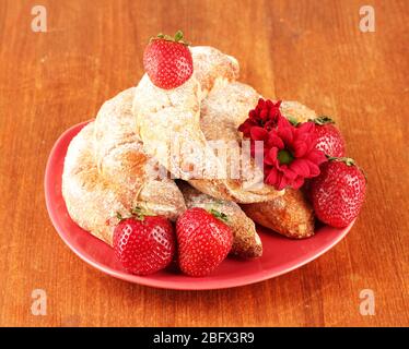 Bagel freschi con fragola nel piatto su sfondo di legno primo piano Foto Stock