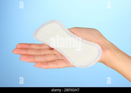 mano della donna che tiene un cuscinetto sanitario quotidiano su sfondo blu primo piano Foto Stock