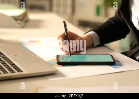 Primo piano delle mani di una donna executive compilando il modulo con lo stilo sullo smartphone di notte in ufficio Foto Stock