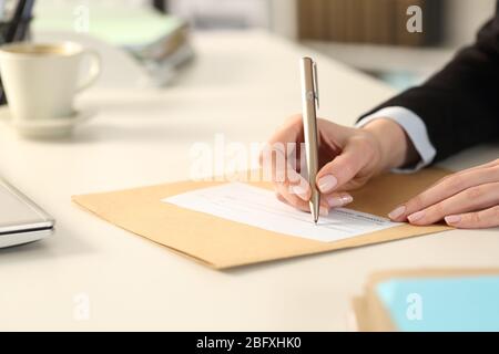 Primo piano della mano della donna d'affari che riempie fuori il controllo della banca che siede su una scrivania all'ufficio Foto Stock