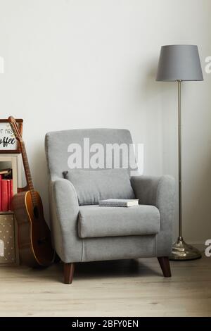 Immagine verticale di una comoda poltrona grigia accanto alla parete bianca in interni di design maschile, spazio copia Foto Stock