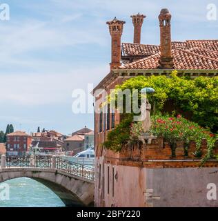 Statua di Santa Maria trovata in un piccolo angolo di strada di Venezia, Italia. Vegetazione verde. Foto Stock