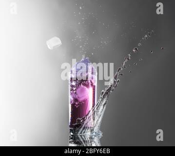 ancora vita di una bevanda rosa in un bicchiere con spruzzi un cubo di ghiaccio volante Foto Stock