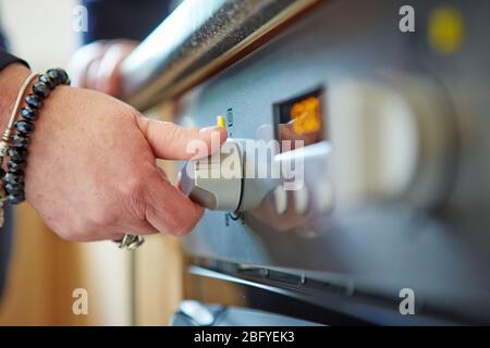 Primo piano di una mano maschile tenendo ruotare il cerchio del quadrante di un forno a microonde per cucinare cibo in cucina a casa Foto Stock