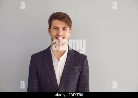 Giovane uomo in giacca sorridente ride allegro felice positivo su sfondo grigio. Foto Stock