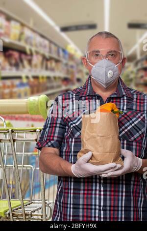 Misure di protezione contro il coronavirus. L'uomo con maschera protettiva, occhiali di protezione e guanti per uso medico trasporta una borsa di verdure fresche su strada della drogheria offuscata Foto Stock