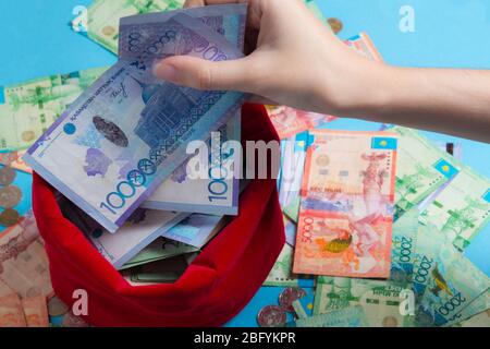 La persona tira i soldi fuori dal sacchetto rosso. KZ. Kazakistan, KZT. Estrarre molto denaro dalla borsa. Moneta nazionale, banconota. Affari, economico Foto Stock