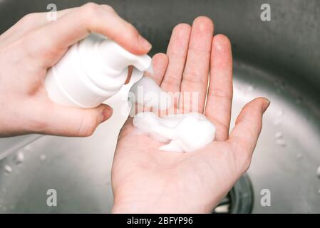 Mettere la bottiglia di sapone di schiuma della frusta con la schiuma sulla mano femmina. Signora che usa il gel di alcool come igienizzante per le mani Foto Stock