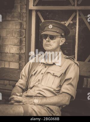 Sepia vintage primo piano di uomo isolato in uniforme militare vintage seduta su panchina, stazione di Arley, Severn Valley Heritage Railway UK, evento estivo degli anni '40. Foto Stock