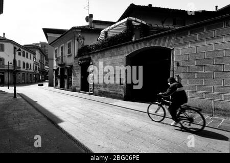 Egli silenzio e la desolazione in una città vicino a Milano, domenica mattina, durante Coronavirus. Nella strada principale del centro città solo un uomo in bicicletta w Foto Stock