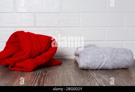 Abbigliamento, moda, stile. Due maglioni su un tavolo di legno. Un maglione rosso rombo e un maglione melange ripiegato con precisione. Ordine e caos. Comfort, pulizia Foto Stock