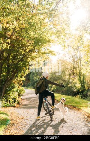 19/4/2020 Donna asiatica con una bici che alimenta un cane in autunno al giardino botanico, Oamaru, Nuova Zelanda. Concetto di esercizio mentre isolamento sociale fr Foto Stock