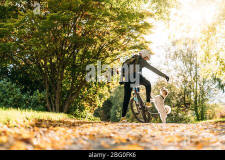 19/4/2020 Donna asiatica con una bici che alimenta un cane in autunno al giardino botanico, Oamaru, Nuova Zelanda. Concetto di esercizio mentre isolamento sociale fr Foto Stock