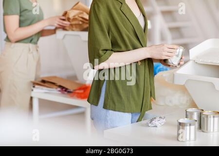 Vista in sezione centrale presso persone non riconoscibili che smistano i materiali di scarto per il riciclaggio a casa, attenzione alla donna che pulisce le lattine metalliche in primo piano, spazio di copia Foto Stock