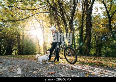 19/4/2020 Donna asiatica con una bici che alimenta un cane in autunno al giardino botanico, Oamaru, Nuova Zelanda. Concetto di esercizio mentre isolamento sociale fr Foto Stock