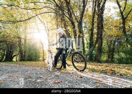 19/4/2020 Donna asiatica con una bici che alimenta un cane in autunno al giardino botanico, Oamaru, Nuova Zelanda. Concetto di esercizio mentre isolamento sociale fr Foto Stock