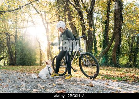 19/4/2020 Donna asiatica con una bici che alimenta un cane in autunno al giardino botanico, Oamaru, Nuova Zelanda. Concetto di esercizio mentre isolamento sociale fr Foto Stock