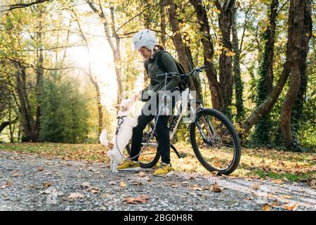 19/4/2020 Donna asiatica con una bici che alimenta un cane in autunno al giardino botanico, Oamaru, Nuova Zelanda. Concetto di esercizio mentre isolamento sociale fr Foto Stock