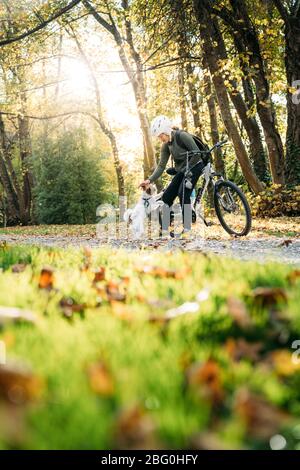 19/4/2020 Donna asiatica con una bici che alimenta un cane in autunno al giardino botanico, Oamaru, Nuova Zelanda. Concetto di esercizio mentre isolamento sociale fr Foto Stock