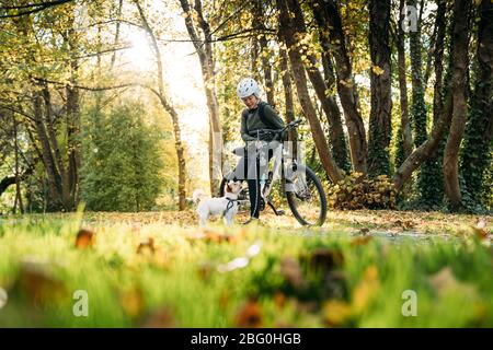 19/4/2020 Donna asiatica con una bici che alimenta un cane in autunno al giardino botanico, Oamaru, Nuova Zelanda. Concetto di esercizio mentre isolamento sociale fr Foto Stock