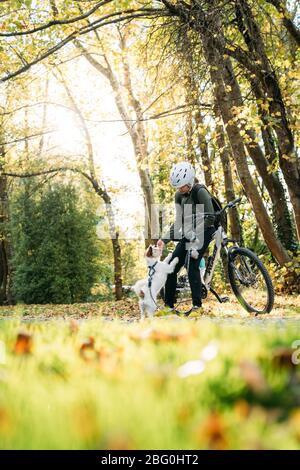 19/4/2020 Donna asiatica con una bici che alimenta un cane in autunno al giardino botanico, Oamaru, Nuova Zelanda. Concetto di esercizio mentre isolamento sociale fr Foto Stock