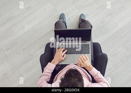 Vista dall'alto di un uomo con un computer portatile seduto su una sedia su uno sfondo grigio. Foto Stock