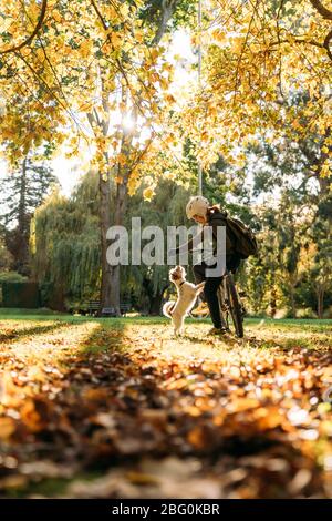 19/4/2020 Donna asiatica con una bici che alimenta un cane in autunno al giardino botanico, Oamaru, Nuova Zelanda. Concetto di esercizio mentre isolamento sociale fr Foto Stock