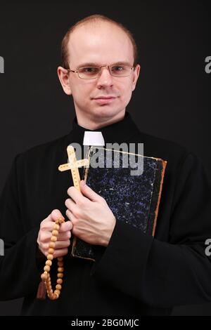 Giovane pastore con croce di legno e Bibbia, isolato su nero Foto Stock