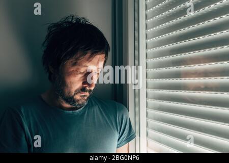 Uomo che si sbroncia dalla finestra con le persiane arrotolate, ritratto di persona maschile deluso Foto Stock