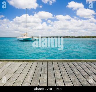 Piattaforma di legno vuota con yacht di lusso ancorato sulle acque turchesi del Mar dei Caraibi sullo sfondo, Repubblica Dominicana Foto Stock