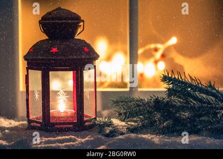 Clise up di una lanterna di Natale illuminata su una davanzale esterno coperto di neve in una notte di neve. Spazio di copia. Foto Stock