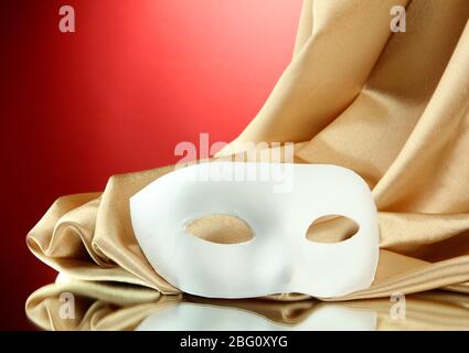 Maschera bianca e tessuto di seta dorata su sfondo rosso Foto Stock