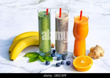 3 diversi tipi di frullati con ingredienti su sfondo tavolo in marmo gigner banana mirtillo spinaci . Foto Stock