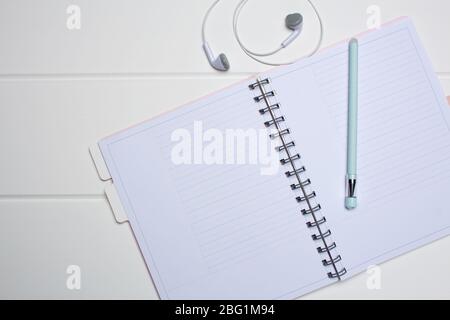 Pianificatore giornaliero su sfondo di legno bianco. Primo piano, spazio per copie, spazio libero, mockup. Foglio pulito, disposizione piatta, vista dall'alto. Blocco note, penna, cuffie Foto Stock