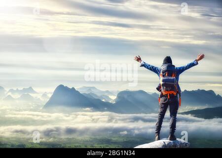 Uomo con zaino, viaggiatore o esploratore in piedi sulla cima di montagna o scogliera e guardando sulla valle. Concetto di scoperta, esplorazione, escursioni, avvento Foto Stock