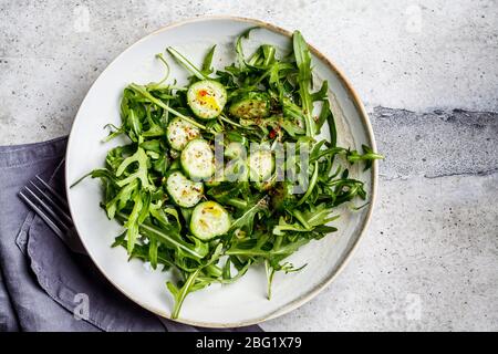 Insalata verde di rucola e cetrioli con olio e spezie in un grande piatto grigio. Foto Stock