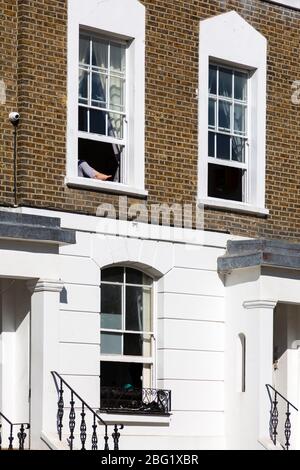 Una donna mette i piedi fuori dalla finestra di un appartamento su Fenniman Road durante la chiusura a Londra a causa della diffusione di Covid-19, 19 aprile 2020 Foto Stock