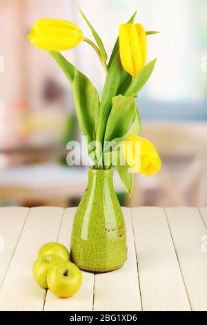 Tulipani gialli in vaso su tavolo di legno sullo sfondo della stanza Foto Stock