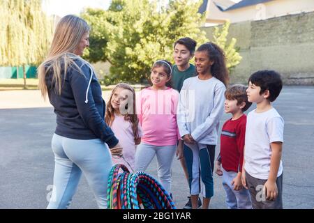 Bambini che fanno educazione fisica in scuola elementare con insegnante di sport nel cortile Foto Stock