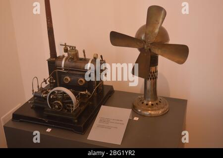 Un motore a vapore vintage accanto a un antico ventilatore elettrico da tavolo in ottone esposto in una collezione museale. Foto Stock