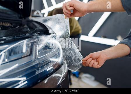 Il lavoratore applica la pellicola di protezione dell'auto sul parafango anteriore Foto Stock