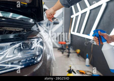 Il lavoratore applica la pellicola di protezione dell'auto sul parafango anteriore Foto Stock